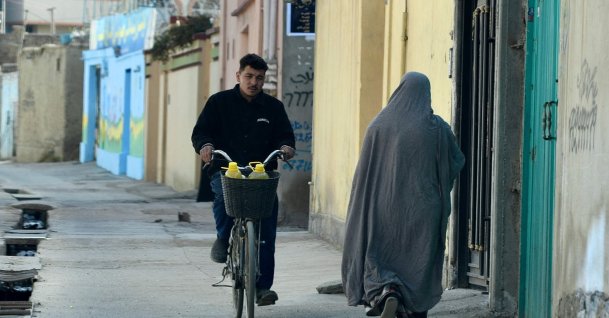 A man rides a bicycle past a woman walking along a street in Kabul, March 19, 2022. (AFP Photo)