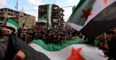 People wave opposition flags at a rally marking 11 years since the start of an anti-regime uprising, in the city of al-Bab in Syria's Aleppo governorate on March 18, 2022 (AFP Photo)