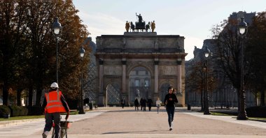 A jogger passes a worker as she runs in front of Arc de Triomphe du Carrousel during a lockdown imposed by authorities in an attempt to halt the spread of the new coronavirus, Paris, Nov. 6, 2020. (AFP Photo)