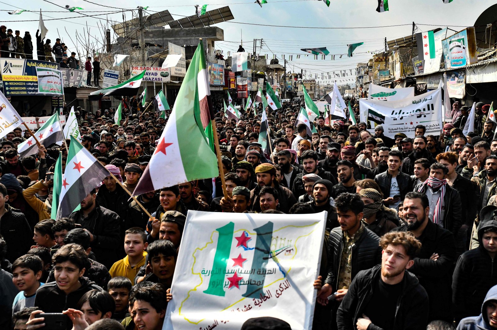 People wave Syrian opposition flags at a rally marking 11 years since the start of an anti-regime uprising, in Afrin in Syria&#039;s opposition-held northern Aleppo province, on March 18, 2022. (Photo by Rami al SAYED / AFP)