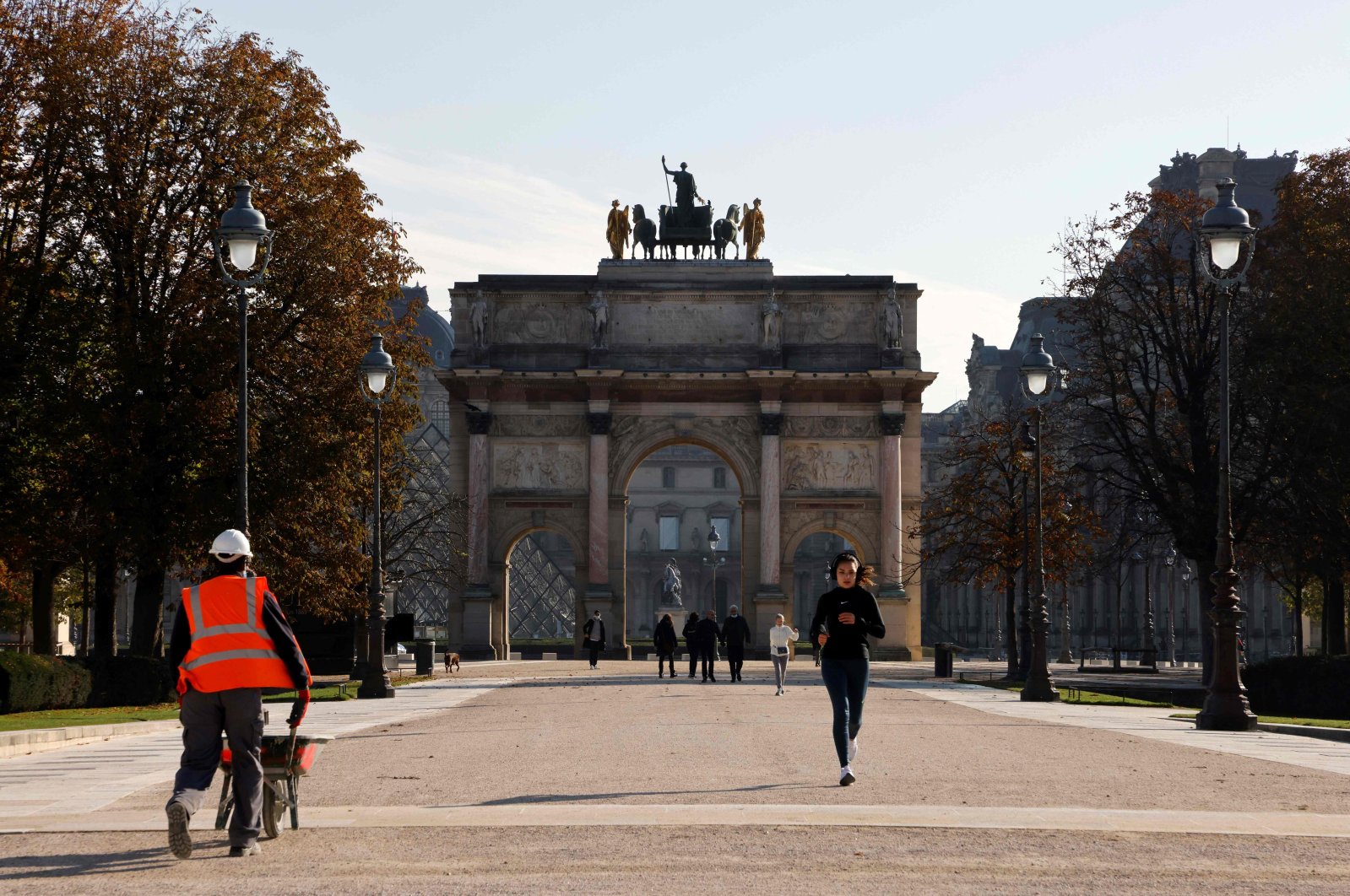 A jogger passes a worker as she runs in front of Arc de Triomphe du Carrousel during a lockdown imposed by authorities in an attempt to halt the spread of the new coronavirus, Paris, Nov. 6, 2020. (AFP Photo)