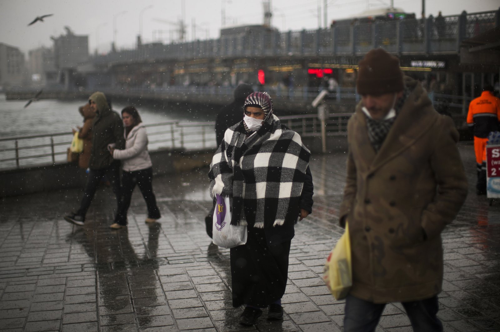 A woman wearing a protective mask against COVID-19 walks next to Galata Bridge, in Istanbul, Turkey, March 19, 2022. (AP PHOTO)