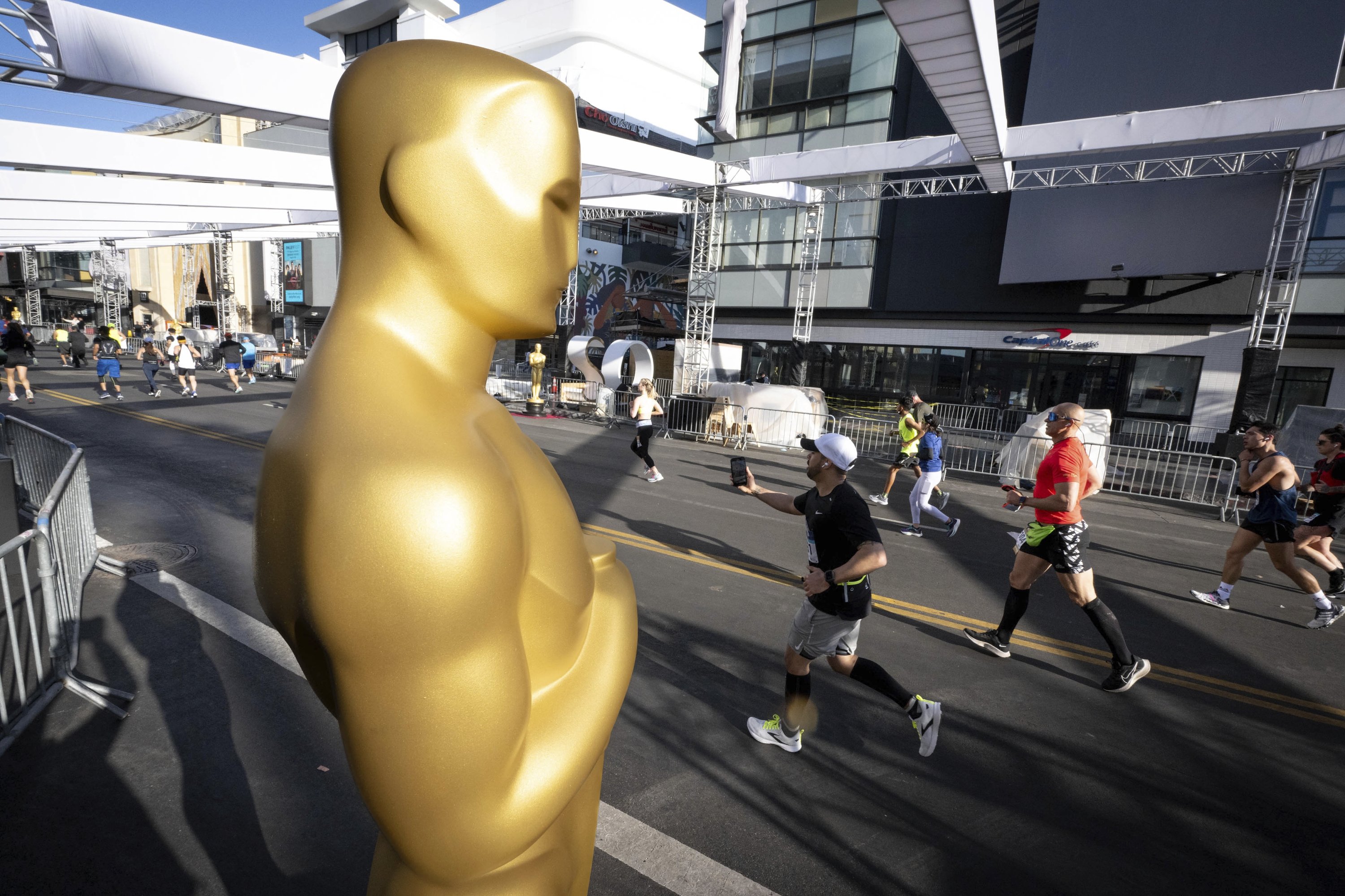 Pelari melewati patung Oscar yang sudah disiapkan untuk Academy Awards 2022 di sepanjang Hollywood Blvd., selama Los Angeles Marathon 2022, California, AS, 20 Maret 2022. (AP Photo)