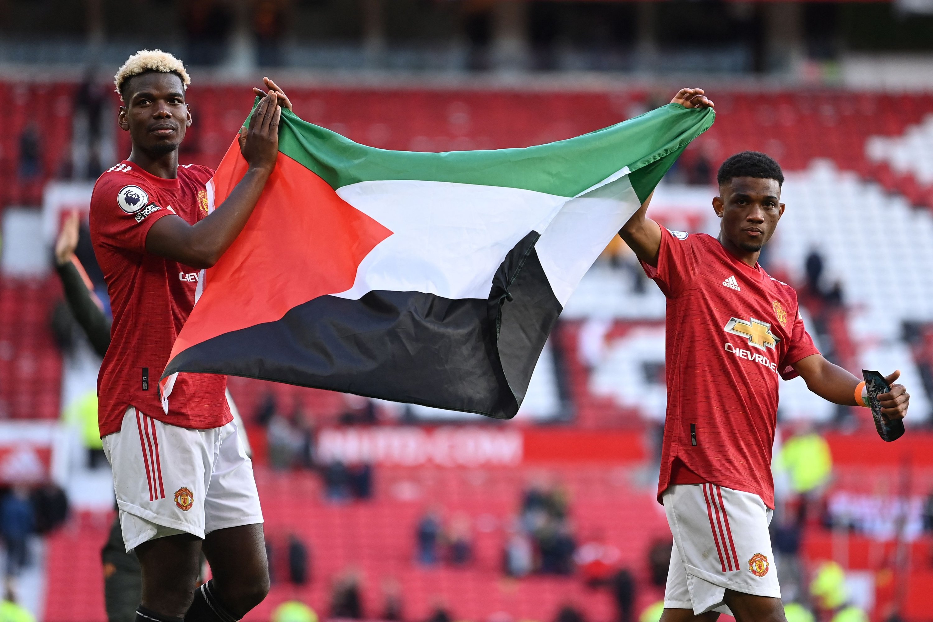 Pemain Manchester United Paul Pogba (kiri) dan Walikota Diallo memegang bendera Palestina saat mereka berjalan di sekitar lapangan pada akhir pertandingan Liga Premier melawan Fulham, Manchester, Inggris, 18 Mei 2021 (AFP Photo)