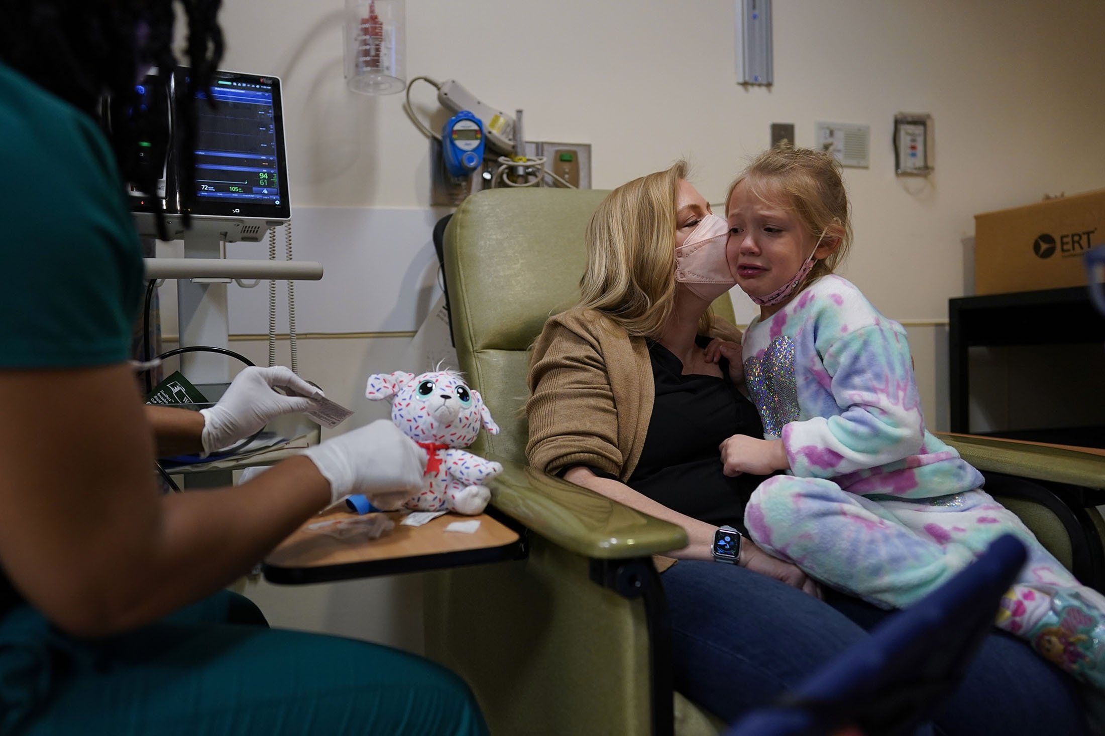 Kate Forte mencium putrinya, Lexie Forte, 6, saat perawat peneliti Michelle Harris, kiri, menunjukkan pengambilan darah pada boneka binatangnya 