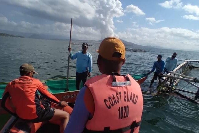 Penjaga Pantai Filipina (PCG) menunjukkan personel penjaga pantai di atas perahu karet membantu nelayan di sebelah gunung berapi Taal yang memuntahkan abu dan uap ratusan meter ke langit di Manila, Filipina, 26 Maret 2022. (EPA Photo)