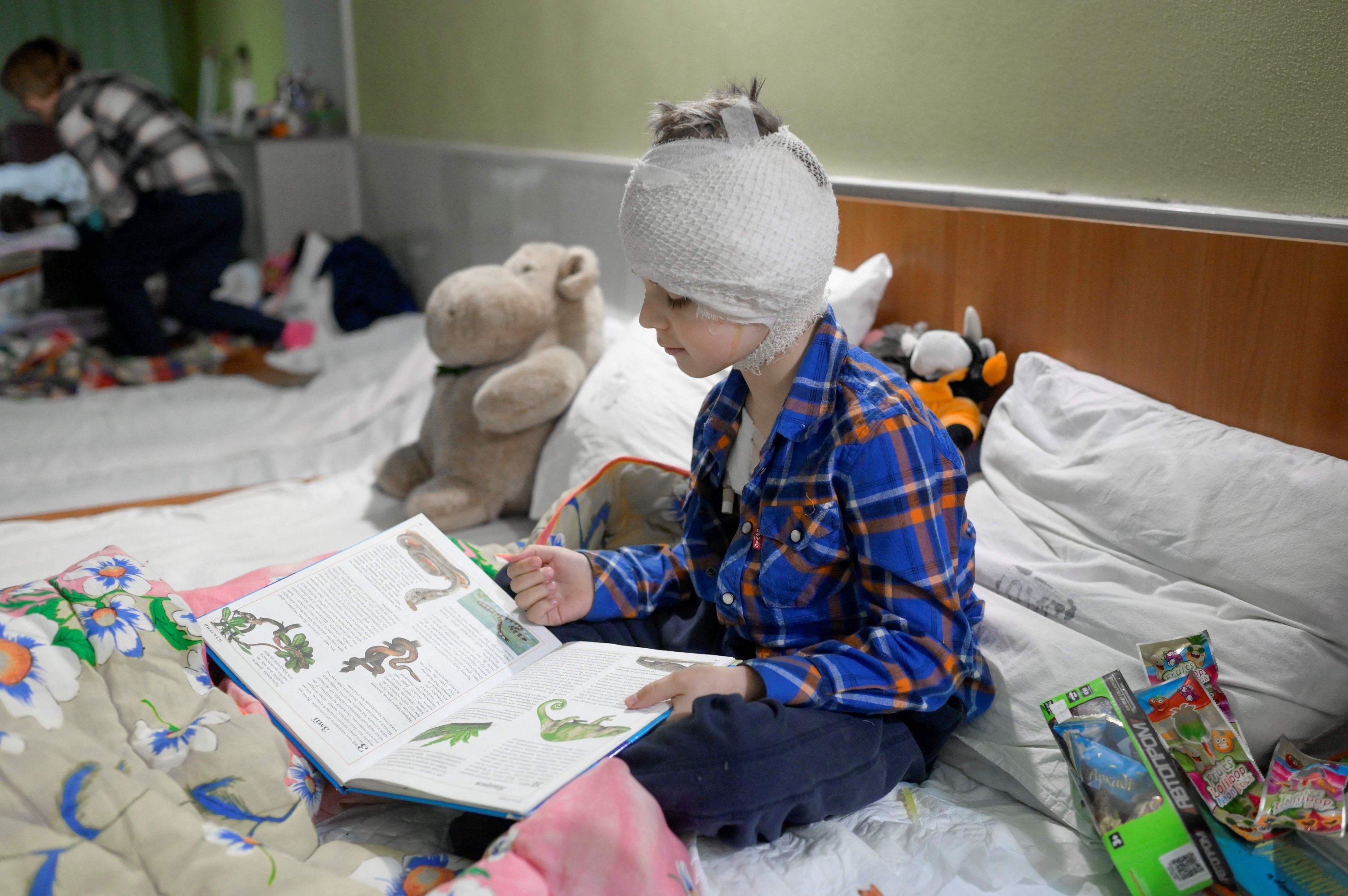 Misha, 5, yang kehilangan ibunya beberapa minggu lalu dan terluka dalam serangan Rusia, membaca buku selama berada di ruang bawah tanah di sebuah rumah sakit, Mykolaiv, Ukraina, 26 Maret 2022. (AFP Photo)