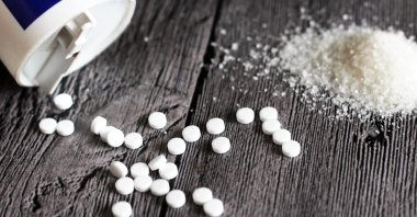 Sweetener tablets besides sugar on wooden table. (Shutterstock Photo)