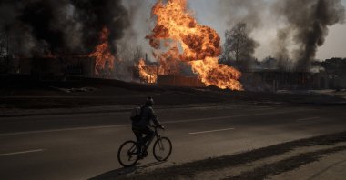 A man rides his bike past flames and smoke rising from a fire following a Russian attack in Kharkiv, Ukraine, March 25, 2022. (AP Photo)