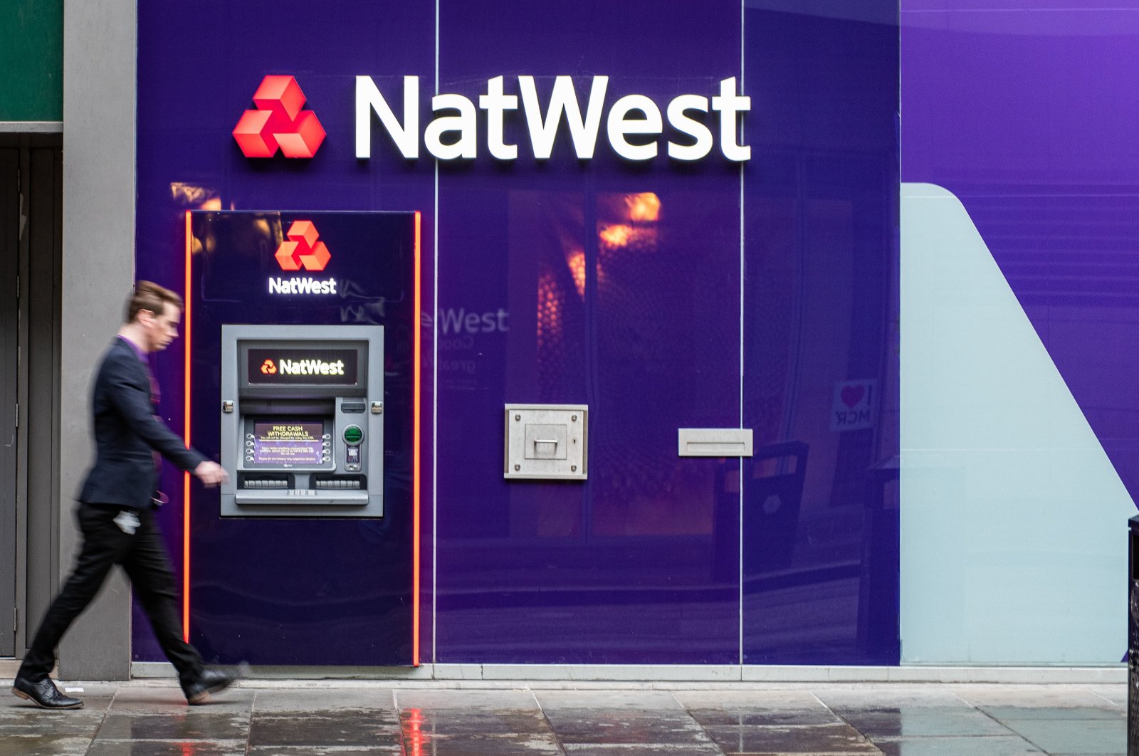 Motion blurred man walks past a Natwest Bank cash machine, Manchester, U.K., July 6, 2019. (Shutterstock Photo)