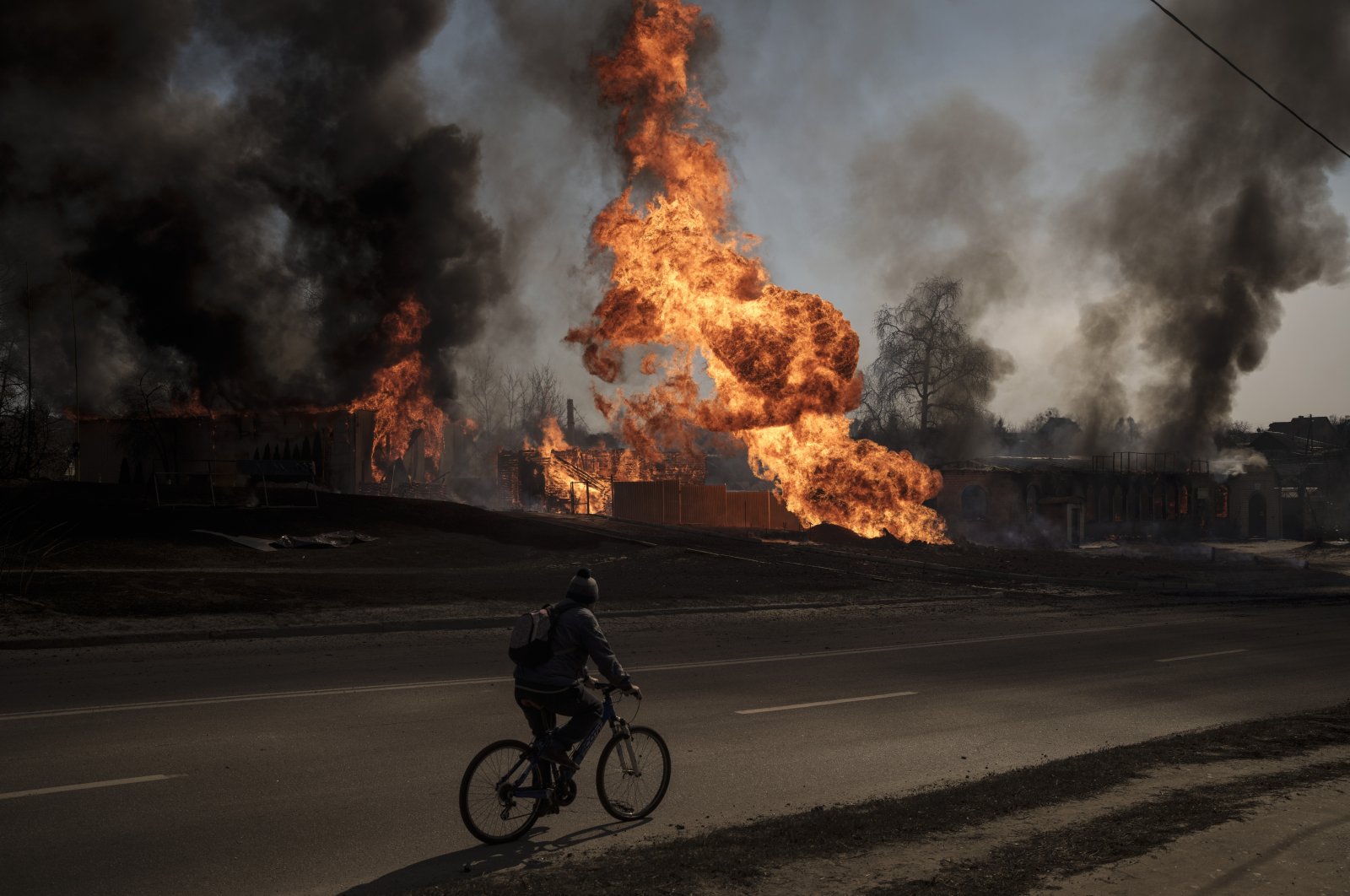 A man rides his bike past flames and smoke rising from a fire following a Russian attack in Kharkiv, Ukraine, March 25, 2022. (AP Photo)