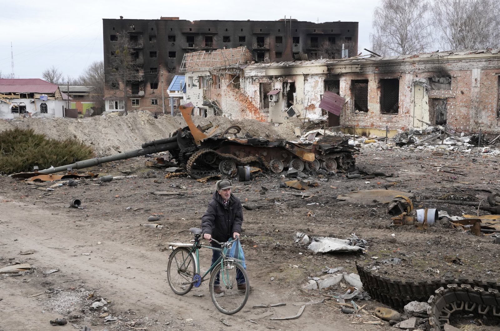 A local resident passes with his bicycle in front of damaged buildings and a tank in the town of Trostsyanets, some 400 kilometers (250 miles) east of the capital Kyiv, Ukraine, March 28, 2022. (AP Photo)