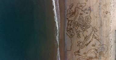 Tide washes away a large sand drawing, depicting an oak leaf, curlew, salmon, and a beaver in the shape of a map of the United Kingdom, in Scarborough, northern U.K., March 23, 2022. (AFP Photo)