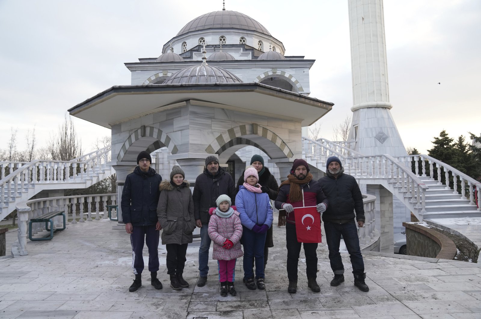 Turkish imam Mehmet Yüce holds a Turkish flag as he poses for a picture with Turkish nationals in front of the mosque in Mariupol, Ukraine, March 12, 2022. (AP Photo)