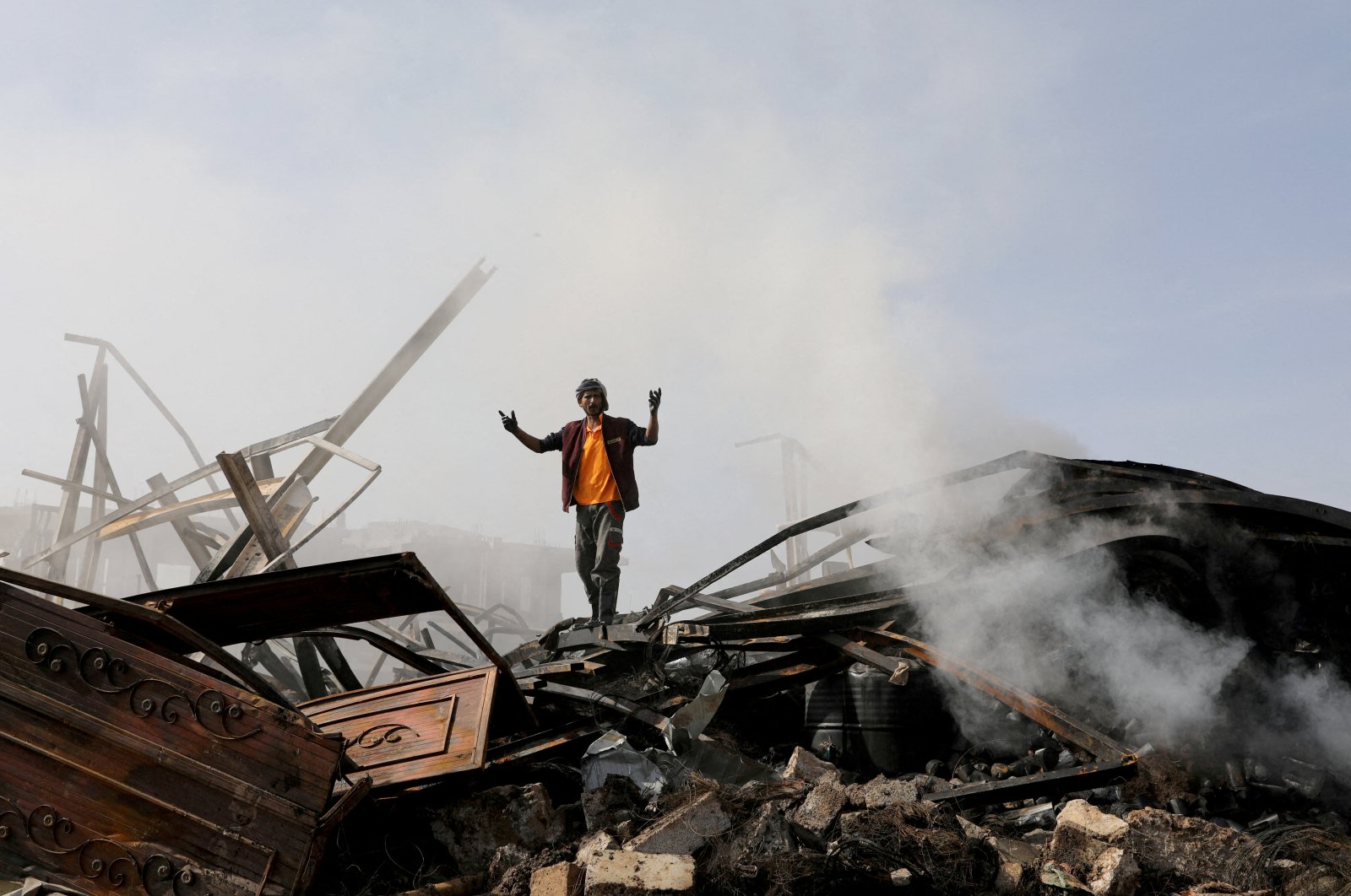 A worker reacts as he stands on the wreckage of a vehicle oil and tires store hit by Saudi-led airstrikes, in Sanaa, Yemen July 2, 2020. (Reuters Photo)
