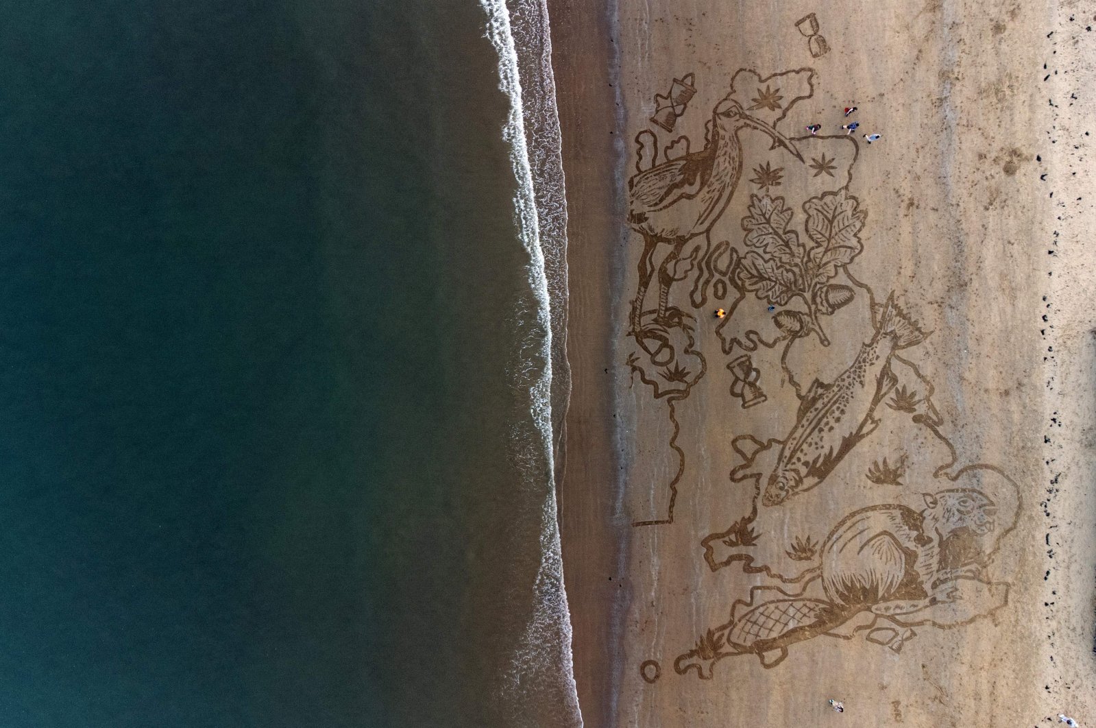 Tide washes away a large sand drawing, depicting an oak leaf, curlew, salmon, and a beaver in the shape of a map of the United Kingdom, in Scarborough, northern U.K., March 23, 2022. (AFP Photo)