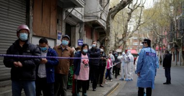 Police officers in protective suits set up cordon next to people lining up to buy food, following COVID-19 outbreak in Shanghai, China, March 30, 2022. (Reuters Photo)