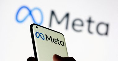 A woman holds a smartphone with the Meta logo in front of a display of Facebook's new rebrand logo Meta in this illustration picture taken on Oct. 28, 2021. (Reuters Photo)