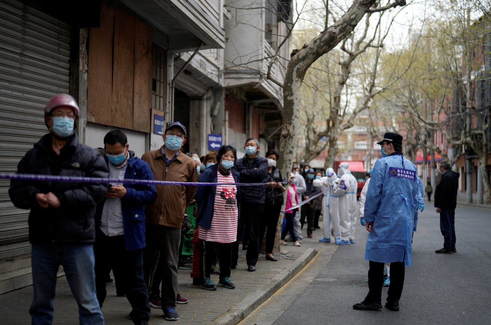 Police officers in protective suits set up cordon next to people lining up to buy food, following COVID-19 outbreak in Shanghai, China, March 30, 2022. (Reuters Photo)