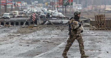 A Ukrainian service member carries a dog next to a destroyed bridge over the Irpin river, as Russia's attack on Ukraine continues, in the town of Irpin, Kyiv region, Ukraine March 30, 2022. (REUTERS)