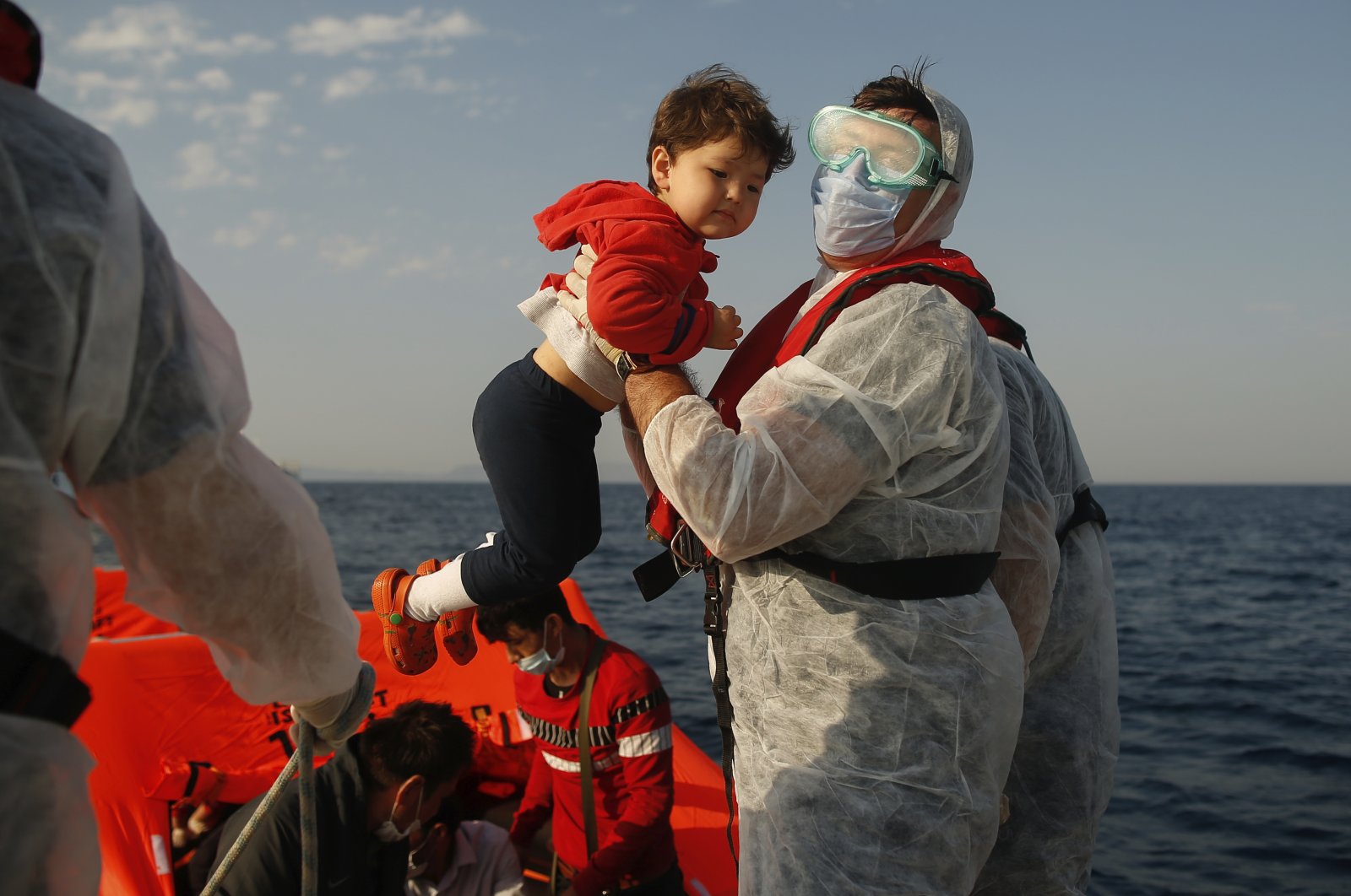 A Turkish coast guard officer, wearing protective gear to help prevent the spread of the coronavirus, lifts a child off a life raft during a rescue operation in the Aegean Sea, between Turkey and Greece, Sept. 12, 2020. (AP File Photo)