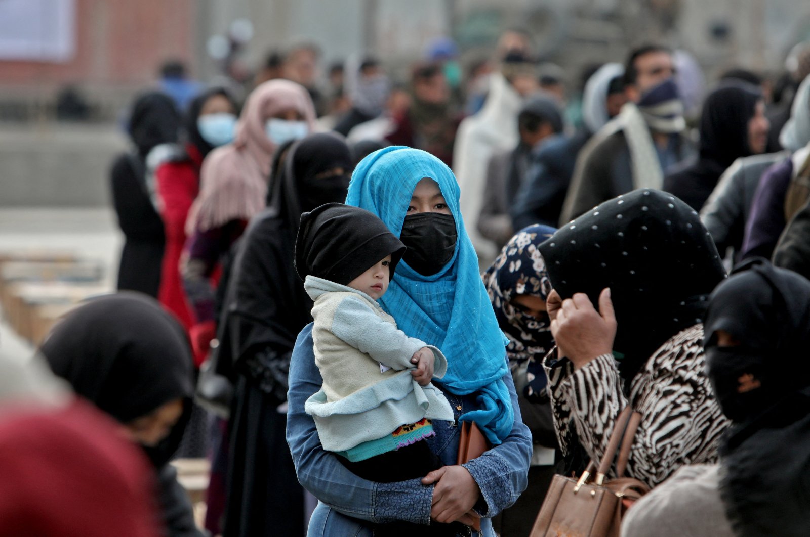 An Afghan woman holds her child as she and others wait to receive a package being distributed by a Turkish humanitarian aid group at a distribution center in Kabul, Afghanistan, Dec. 15, 2021. (Reuters Photo)