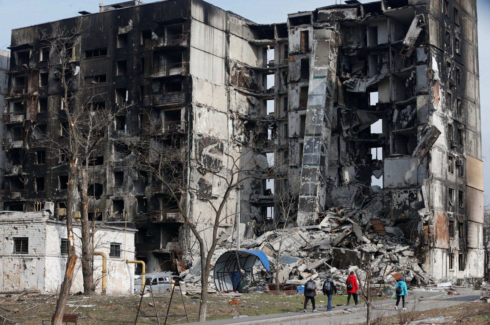 Local residents walk near an apartment building destroyed during the Ukraine-Russia conflict in the besieged southern port city of Mariupol, Ukraine, March 30, 2022. (Reuters Photo)