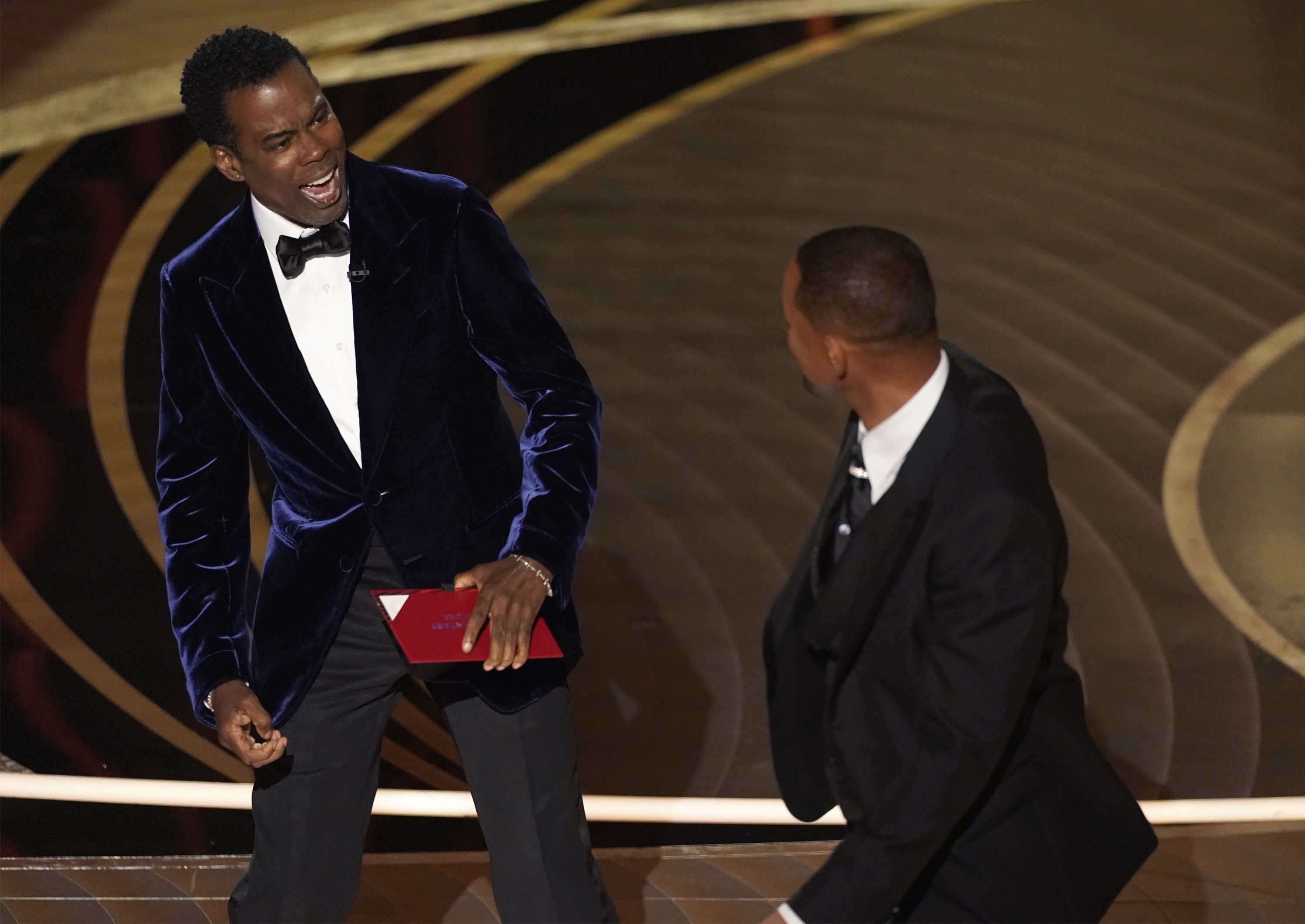 Presenter Chris Rock (kiri) bereaksi setelah dipukul di atas panggung oleh Will Smith saat mempersembahkan penghargaan untuk film dokumenter terbaik di Oscar pada hari Minggu, 27 Maret 2022, di Dolby Theatre di Los Angeles.  (AP)