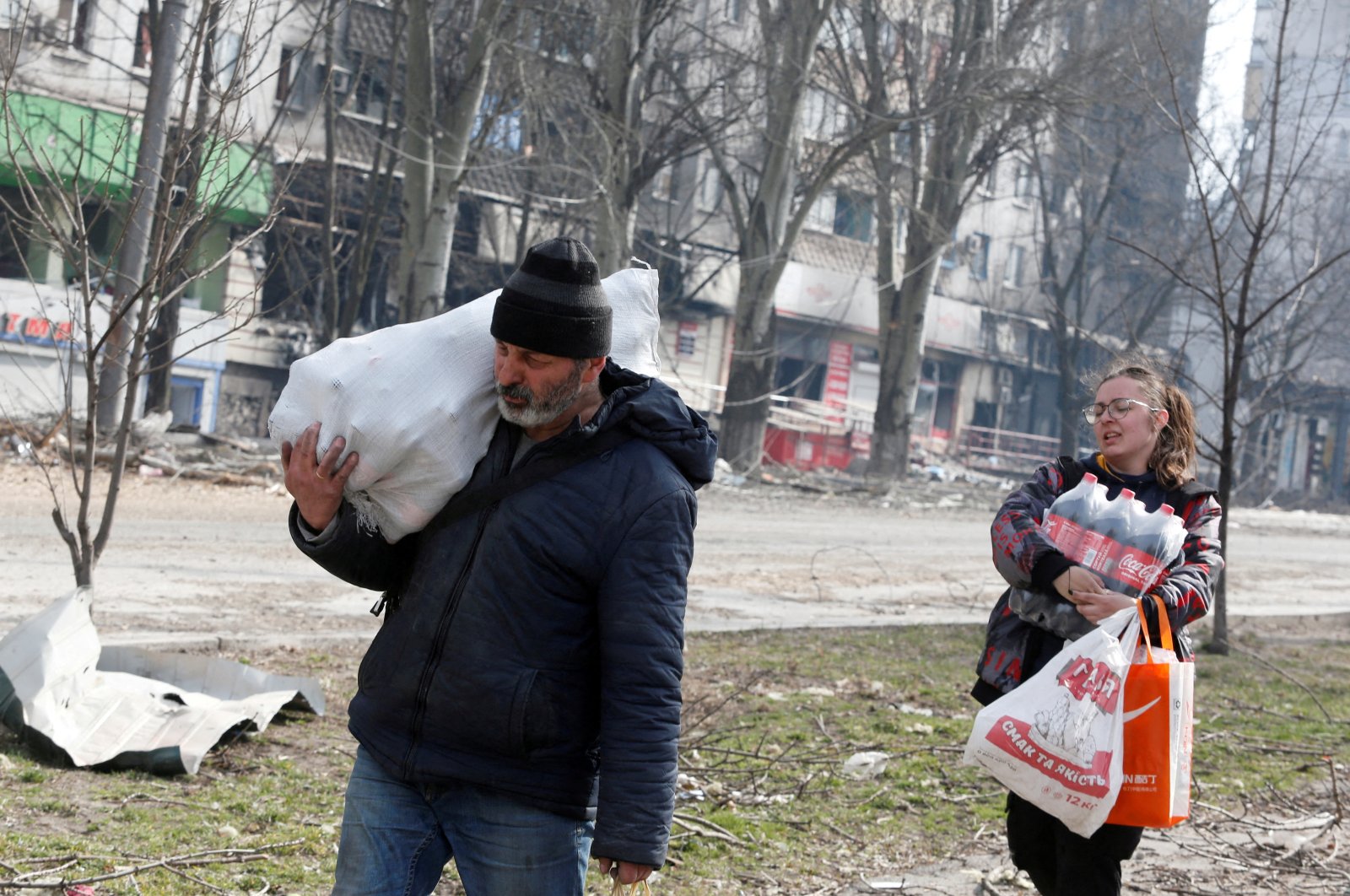 Local residents carry foodstuff while walking past an apartment building damaged during the Ukraine-Russia conflict in the besieged southern port city of Mariupol, Ukraine March 31, 2022. (REUTERS)