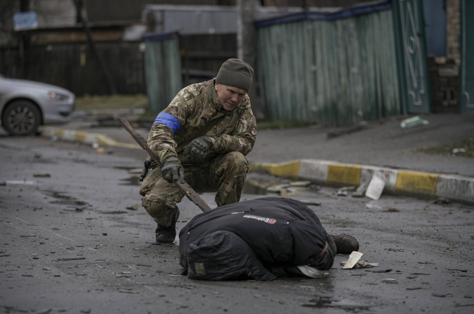 A Ukrainian soldier uses a piece of wood to check if the body of a man dressed in civilian clothing is booby-trapped with explosive devices, in the formerly Russian-occupied Kyiv suburb of Bucha, Ukraine, April 2, 2022. (AP Photo)