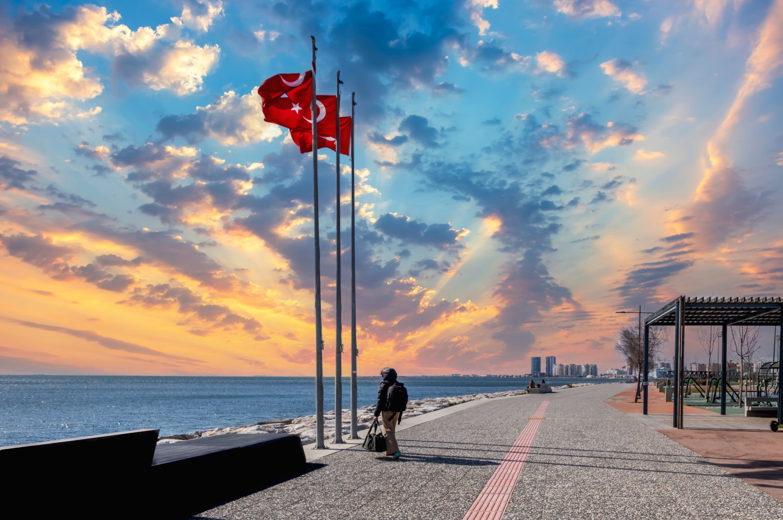 A man standing near waving Turkish flags spends time at the seaside in the Bostanlı district, Izmir, western Turkey, March 18, 2022. (Photo by Shutterstock)