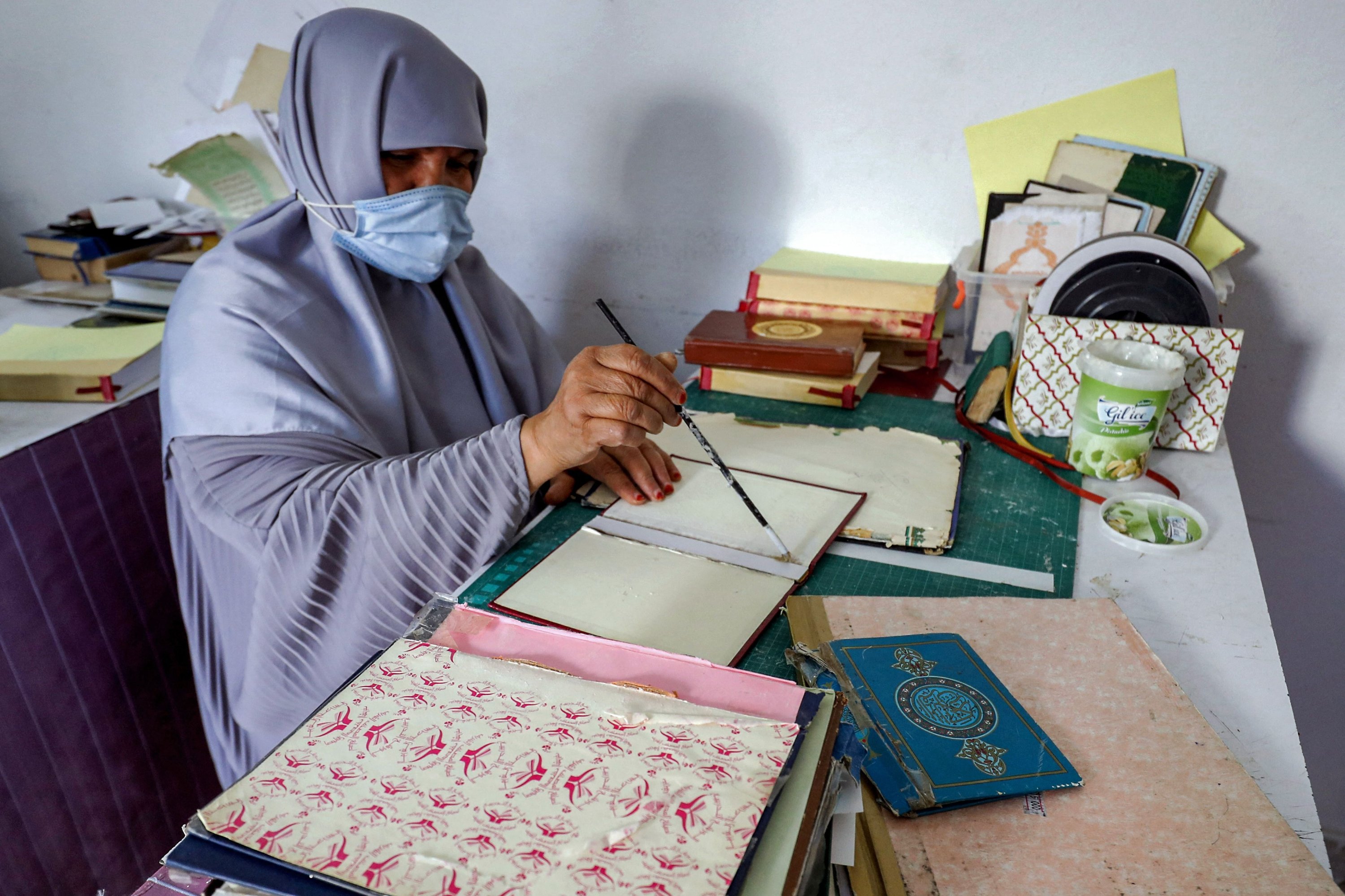 Seorang wanita mengoleskan lem pada hardcover yang mengikat satu volume Al-Qur'an, kitab suci Islam, selama lokakarya pemulihan salinannya di ibu kota Libya, Tripoli, 22 Maret 2022. (AFP Photo)
