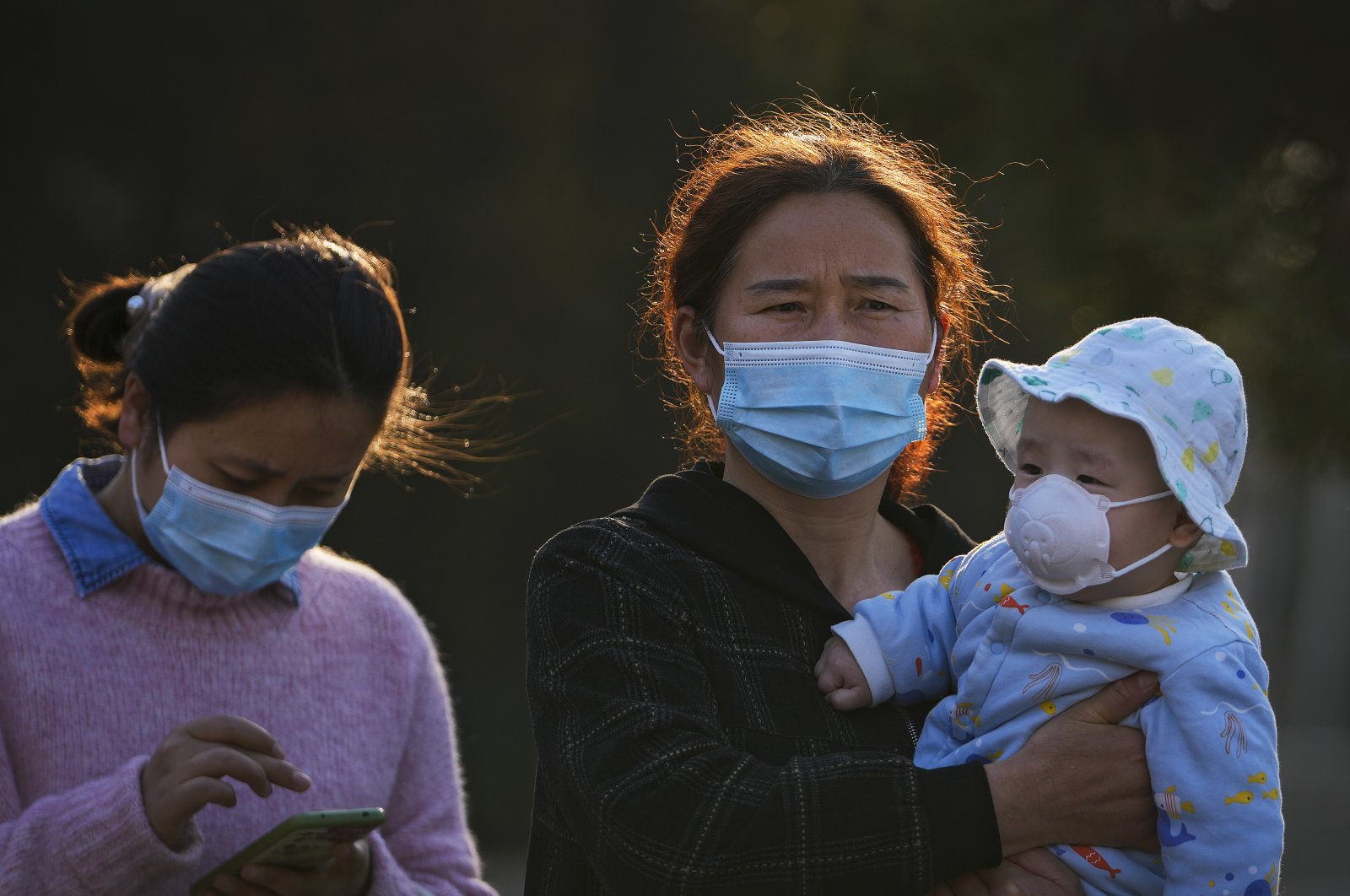 Residents wearing face masks to help protect from the coronavirus bring a masked child to visit a park in Beijing, China, April 3, 2022. (AP Photo)