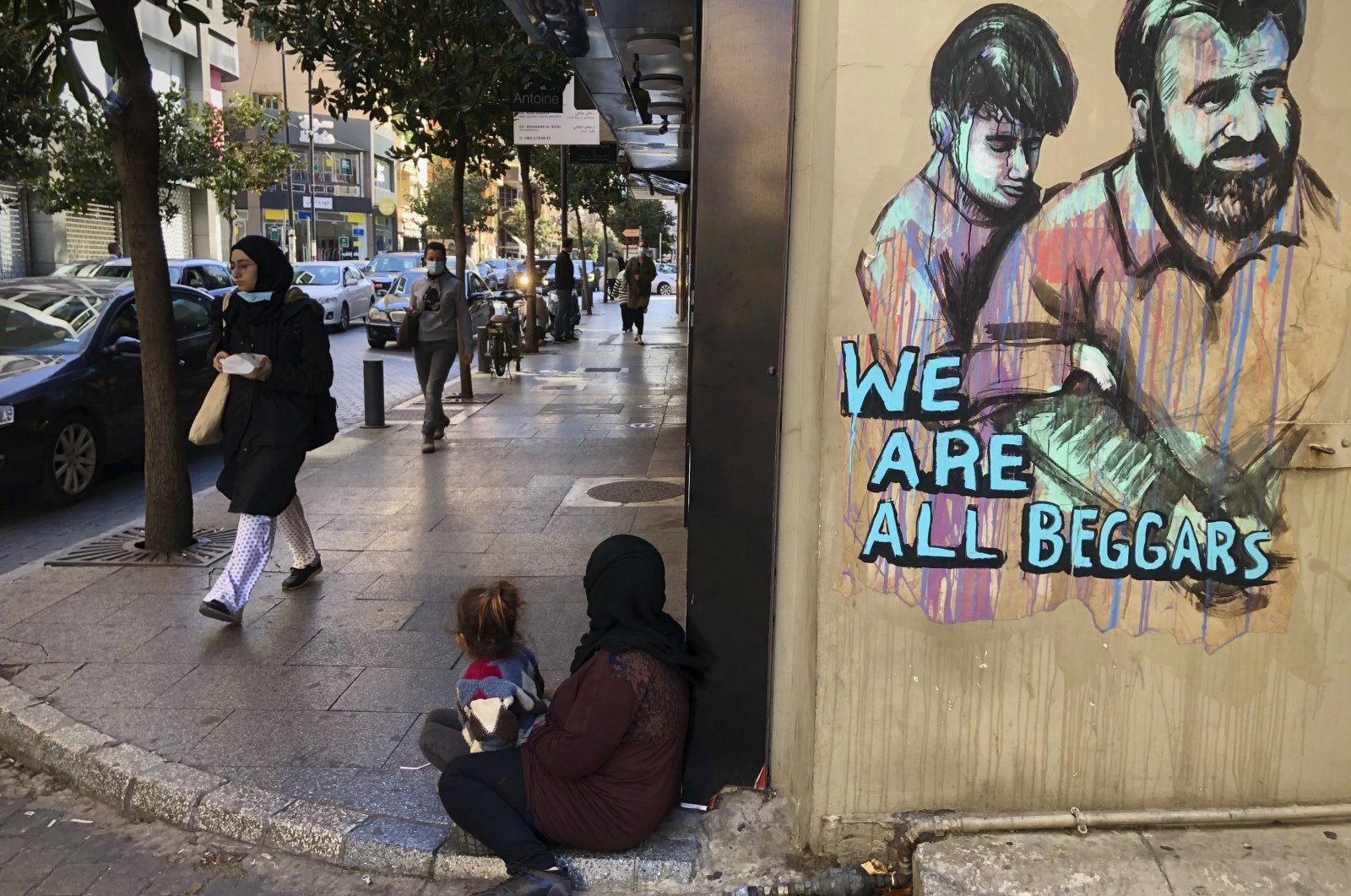 Passersby walk by a woman (C) sitting on the ground with her daughter begging on Beirut&#039;s commercial Hamra Street, Beirut, Lebanon, March 16, 2021. (AP Photo)
