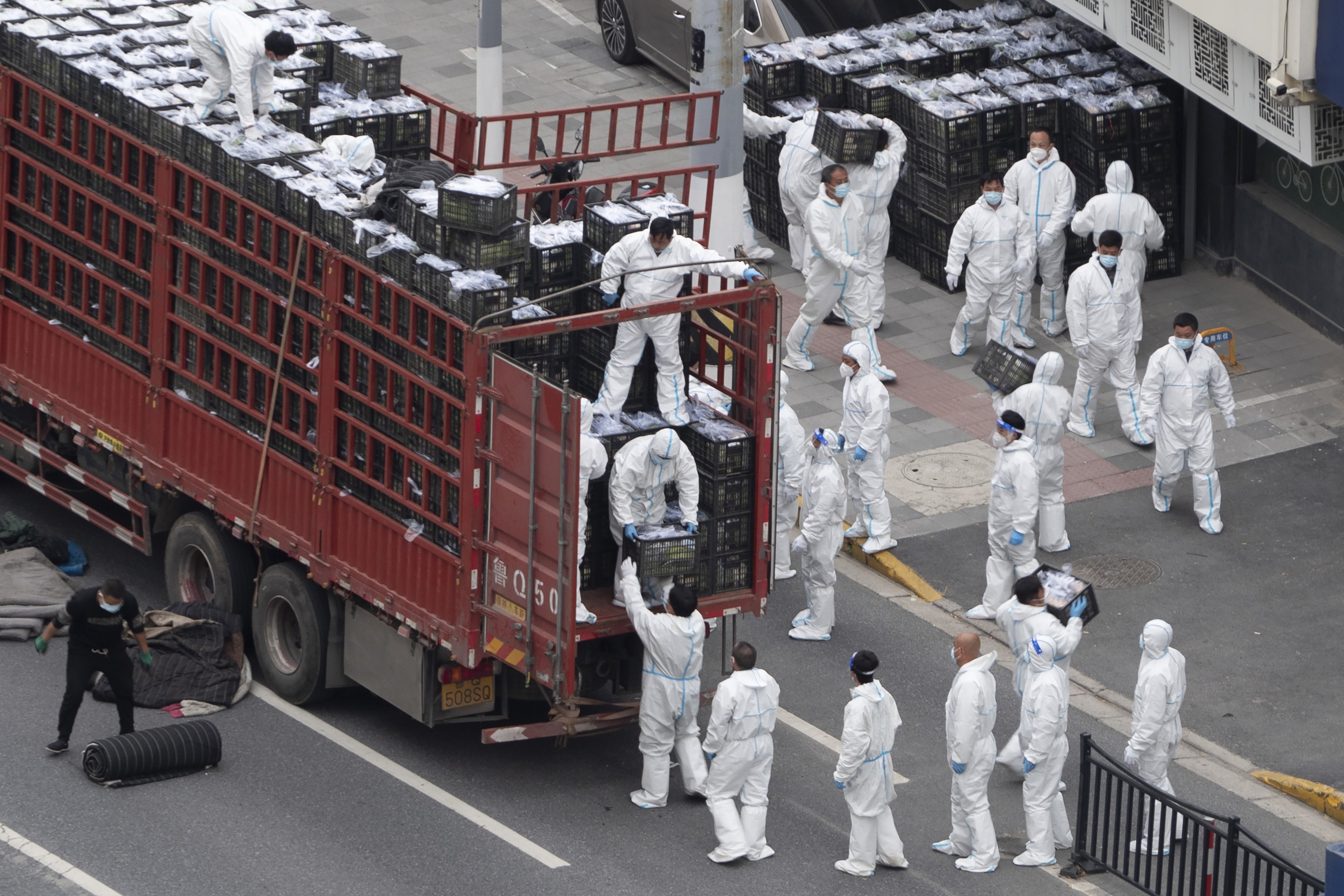 Workers in PPE unload groceries from a truck before distributing them to local residents under the COVID-19 lockdown in Shanghai, China, April 5, 2022. (Photo via AP)