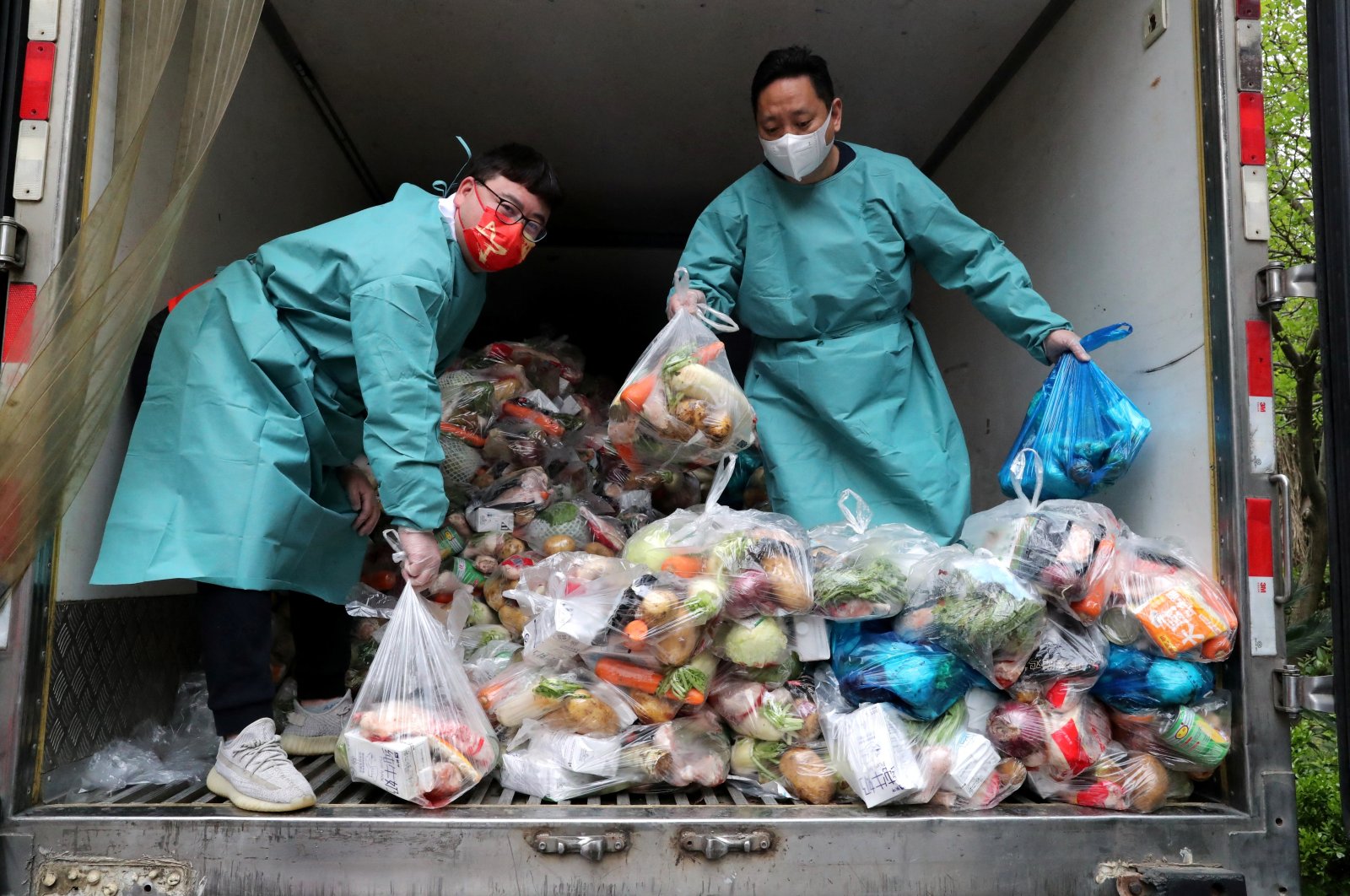 Workers wearing protective gear sort bags of vegetables and groceries on a truck to distribute them to residents at a residential compound, during the lockdown to curb the coronavirus outbreak in Shanghai, China, April 5, 2022. (China Daily via Reuters)