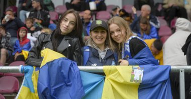 Ukrainian supporters pose next to the Ukrainian flag during the European Youth League round of 16 soccer match between Dynamo Kyiv U19 and Sporting CP U19, at the Giulesti stadium in Bucharest, Romania, April 7, 2022. (AP Photo)