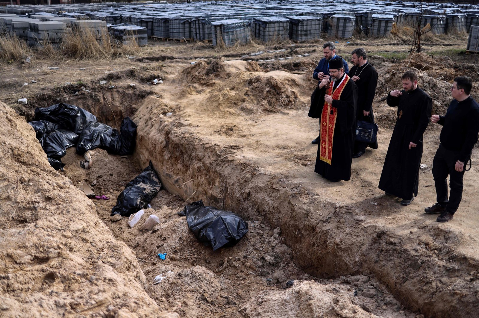 Priests pray near body bags in a mass grave in the garden surrounding the St. Andrew church in Bucha amid Russia&#039;s military invasion of Ukraine, April 7, 2022. (AFP Photo)
