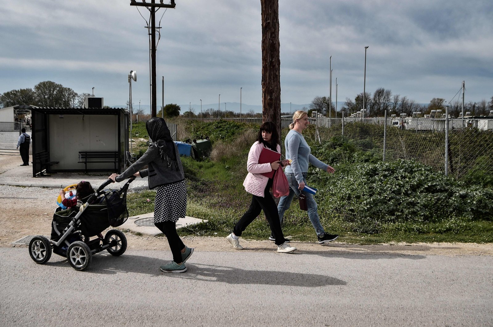 Ukrainian refugees (R) walk next to a migrant woman from Afghanistan with her baby (L) at Serres refugee camp, northern Greece, April 4, 2022. (AFP Photo)