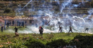 Palestinians run for cover during clashes with Israeli security forces at the northern entrance of Ramallah, near the Israeli settlement of Beit Eil, in the occupied West Bank, April 11, 2022. (Photo by ABBAS MOMANI via AFP)