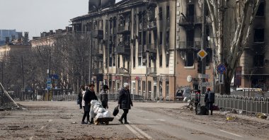 Residents carry their belongings across a street near a building burnt in the course of the Ukraine-Russia conflict, in the southern port city of Mariupol, Ukraine, April 10, 2022. (Reuters Photo)