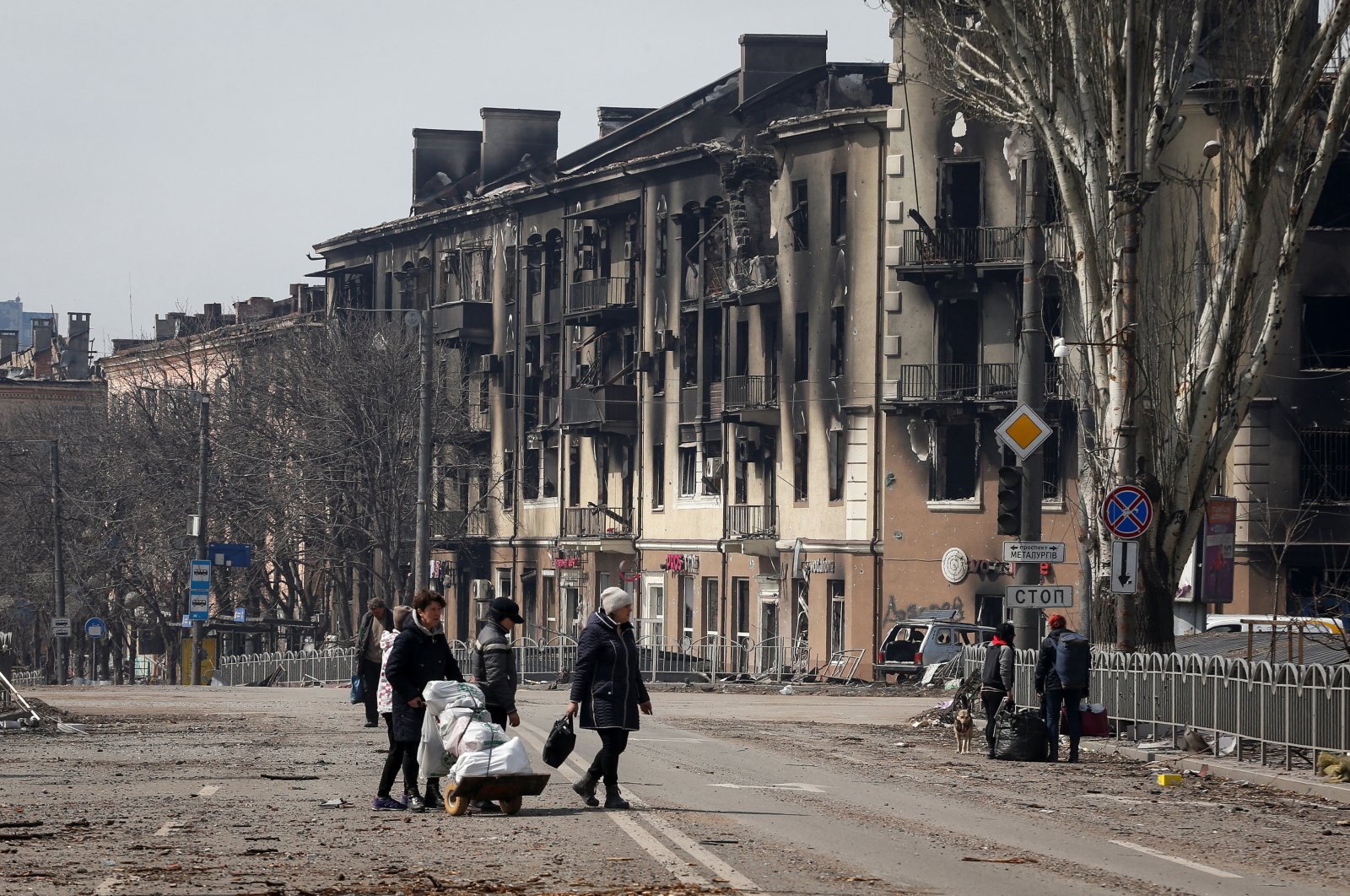 Residents carry their belongings across a street near a building burnt in the course of the Ukraine-Russia conflict, in the southern port city of Mariupol, Ukraine, April 10, 2022. (Reuters Photo)