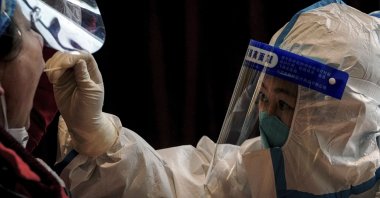 A health worker in protective suit takes a throat swab sample from a worker at a coronavirus testing site inside a hotel, in the Yanqing district of Beijing, China, March 17, 2022. (AP Photo)