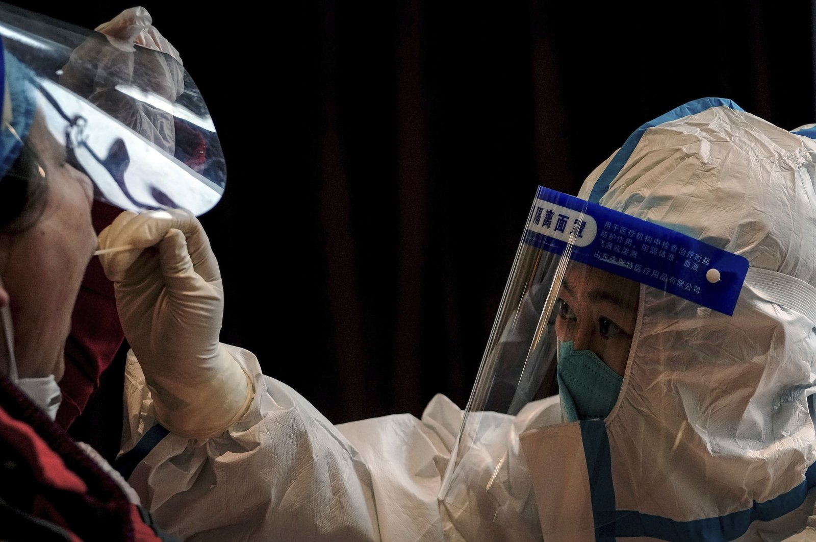 A health worker in protective suit takes a throat swab sample from a worker at a coronavirus testing site inside a hotel, in the Yanqing district of Beijing, China, March 17, 2022. (AP Photo)