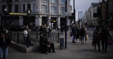 A man sits next to a London Underground sign for Oxford Circus station, on the Oxford Street shopping district, in London, April 1, 2022. (AP Photo)