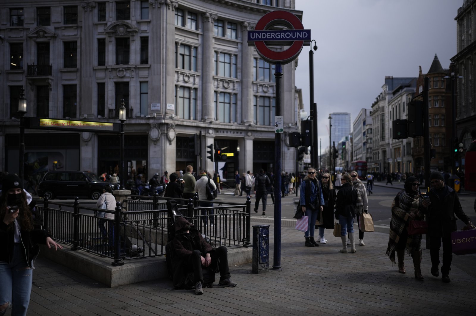 A man sits next to a London Underground sign for Oxford Circus station, on the Oxford Street shopping district, in London, April 1, 2022. (AP Photo)