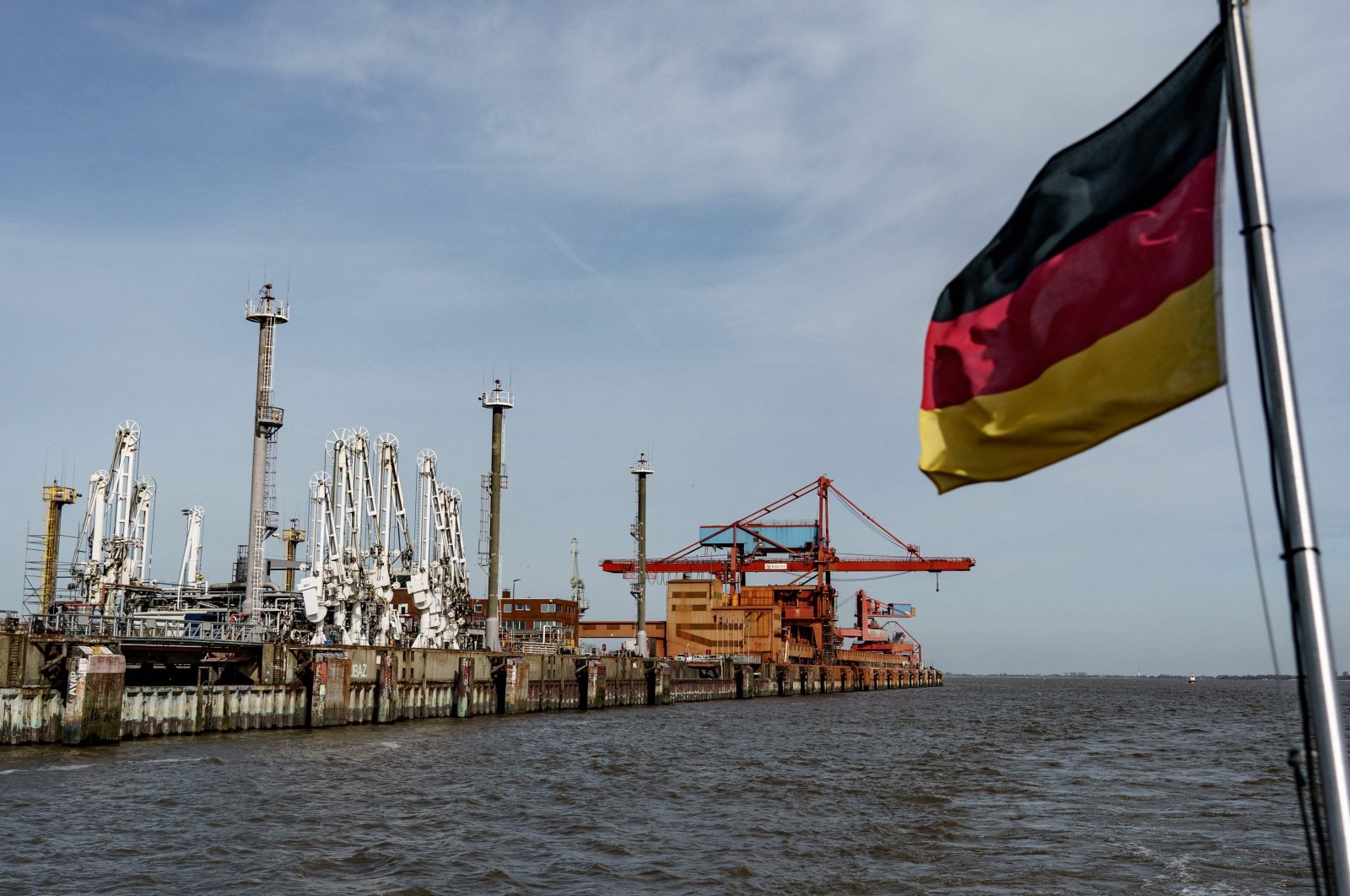 A German flag waves from the back of a ship in front of port facilities at the industrial harbor of Stade, on the river Elbe in northern Germany, April 12, 2022. (AFP Photo)