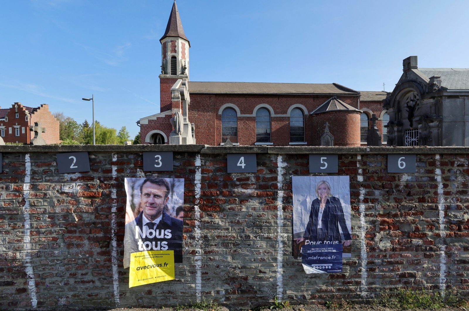 Official campaign posters of French presidential election candidates Marine le Pen, leader of French far-right National Rally (Rassemblement National) party, and French President Emmanuel Macron, candidate for his re-election, displayed on a cemetery wall in Aubencheul-au-Bac, France, April 16, 2022. (REUTERS)