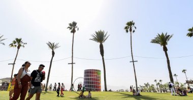 People sit in the shade of palm trees at the Coachella Valley Music and Arts Festival in Indio, California, April 16, 2022. (AFP Photo)