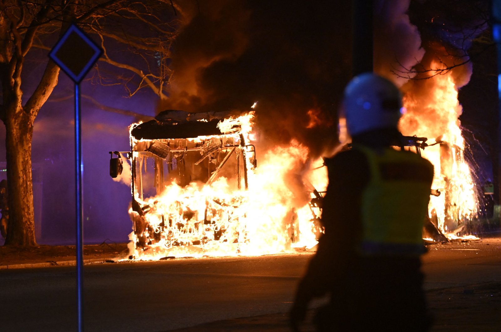 An anti-riot police officer stands next to a city bus burning in Malmo, Sweden, April 16, 2022. (AFP Photo)
